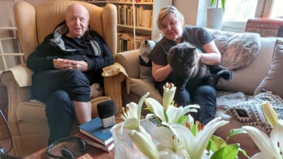 Katten Felix sitter i författaren Carina Nynäs famn. Hon sitter i soffan och bredvid henne i en länstol sitter hennes författarman Lars Bergquist.