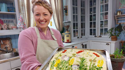 En leende kvinna i ett kök håller i en plåt med foccacia