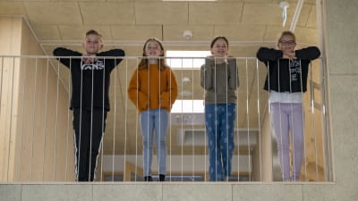 Fyra skolelever står på övre våningen i ett nybyggt skolhus och tittar ner.