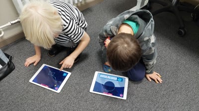 Kaksi lasta pelaa maassa tabletilla Pikku Kakkosen Eskarin Tähtitiedettä.