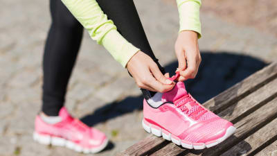En kvinna knyter skosnöret på sina rosa löparskor.