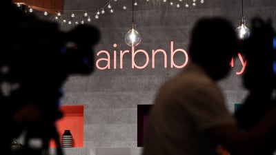 Aibnb:s logga på en vägg med skuggor av personer i fögrunden.