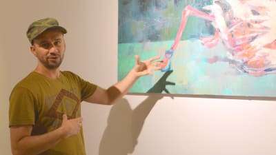 En man står vid sin målning som föreställer en flamingo med fastbundna ben.