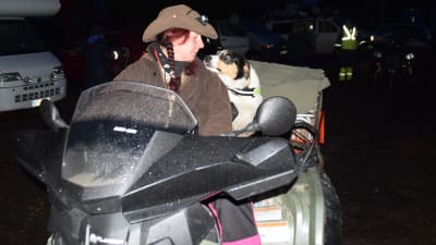 En kvinna i hatt och en hund på en fyrhjuling. Det är mörkt som på natten ute.