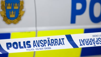 Närbild på platsband där det står "polis avspärrat" framför en svensk polisbil.