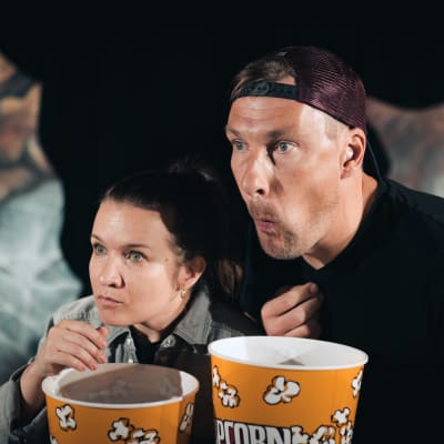 En man och en kvinna med popcornaskar i händerna följer spänt något med blicken. 