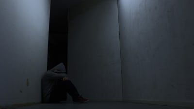 En ung kille sitter ensam i ett kalt rum.