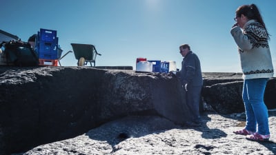En man och en kvinna på klippor tillsammans med plastbackar med saker, vattendunkar och en skottkärra.