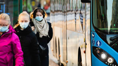 Ihmisiä hengityssuojaimet kasvoilla bussipysäkillä Sörnäisissä.