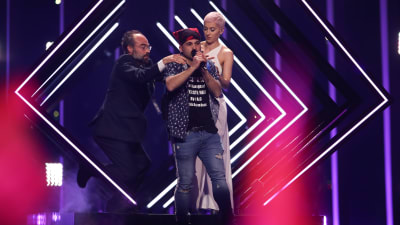 En ordningsvakt försöker fösa ner en person från Eurovisionsscenen medan brittiska Surie ser på.