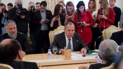 Män samlade vid ett bord. Sergej Lavrov i mitten och Adam Delimkhanov till vänster. I bakgrunden journalister.