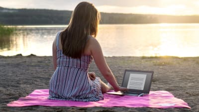 En ung kvinna sitter på stranden med en laptop.