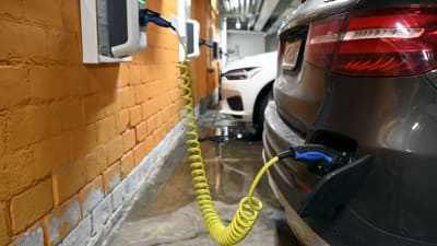 Närbild på laddstation och elbil som laddas vid station i garage.