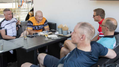 Fem manliga cyklister sitter vid ett bord på en uteservering.