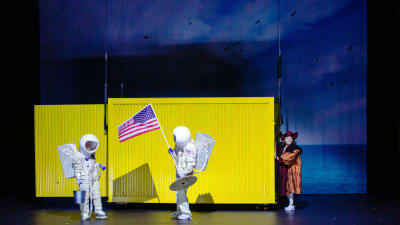 Två gestalter i rymddräkt står framför en gul fraktcontainer.