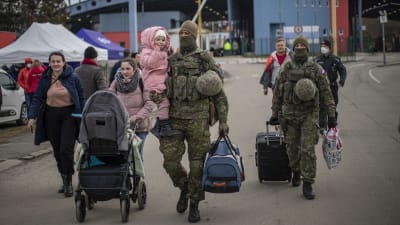 Soldater går bredvid flyktingar från Ukraina. En av soldaterna håller i ett litet barn.