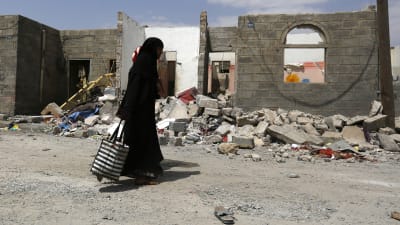 Kvinna går förbi ett hus som förstörts i en saudiledd lufträd.
