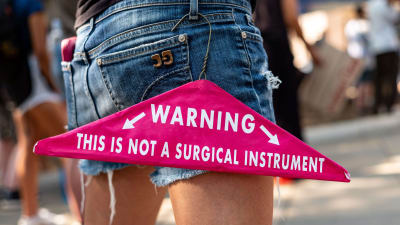 En klädgalge hänger från en persons ficka. På galgen står det "Varning, det här är inget kirurgiskt verktyg".