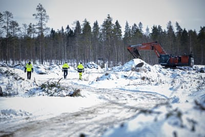 Tre män i arbetskläder går omkring på gruvdriftsområde. Snö ligger på marken och en grävmaskin syns i bakgrunden.