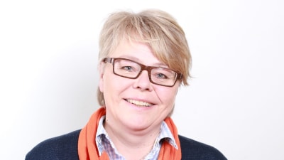 En glad kvinna med kort ljust hår och glasögon tittar in i kameran.