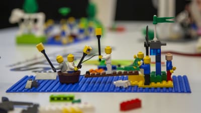 Legogubbar åker i en tunna framför en legoö med brygga. 