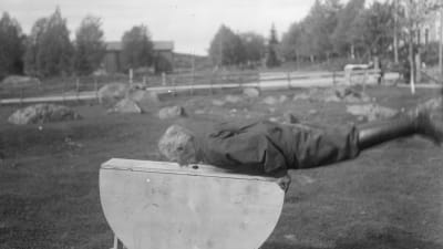 En man leker leken "taga pengen från bordet med munnen". Bilden är tagen 1930 i Närpes, Kalaks.