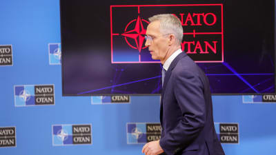 Jens Stoltenberg i profil framför Natos logotyp på en skärm.