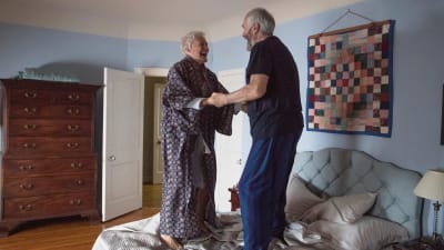 Joan (Glenn Close) och Joe (Jonathan Pryce) håller varandra i händerna och hoppar på sängen av glädje.