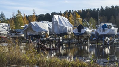Flera båtar står förvarade på ställningar på land. Marken är täckt av vatten.