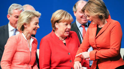 Ursula von der Leyen, Angela Merkel och Julia Klöckner står bredvid varandra och skrattar och jämför de olika röda nyanserna på deras kavajer.