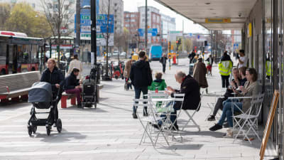 Stadsbild från Stockholm med folk som promenerar på gatan och sitter på uteservering.