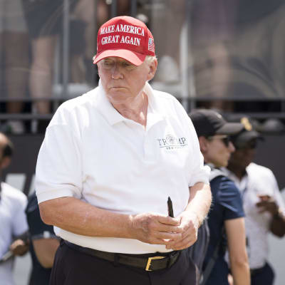 En man i vit t-skjorta och röd keps, med en golfklubba i handen.