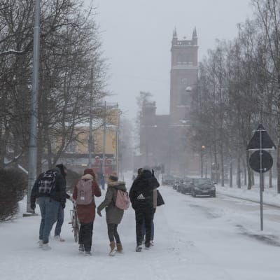 Fotgängare på trottoaren i snöoväder. I bakgrunden Trefaldighetskyrkan i Vasa. 