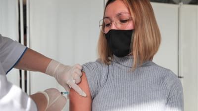 En ung kvinna i munskydd får coronavaccin.