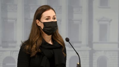 Sanna Marin på presskonferensen framför podiet i svart klänning och utsläppt hår. 