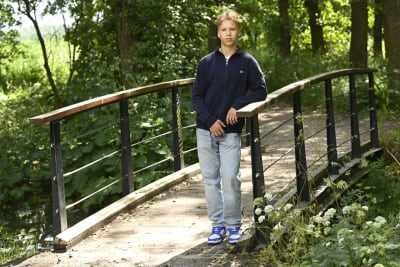 Tonårig pojke står på en bro i skogsdunge.