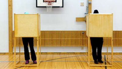 Två personer står i varsitt väljarbås och röstar.