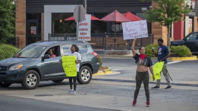 Två kvinnor med varsin skylt med slogans mot polisbrutalitet står utanför en restaurang och protesterar.