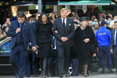 Kung Willem-Alexander och drottning Maxima samt Beatrix av Nederländerna går mot kyrkan. Bakom dem syns poliser som håller allmänheten på avstånd.
