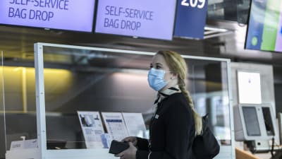 En kvinna med ansiktsskydd och Finnairs uniform står framför en check-in-disk.