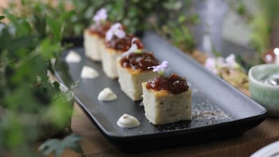 Fyra bitar rispannkaka på svart serveringsfat dekorerade med aprikoskompott och blommor.