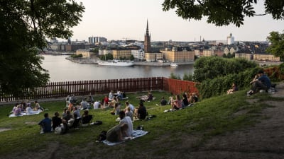 Människor sitter i Ivar Los Park i Stockholm. En vy över staden syns vid vattnet.