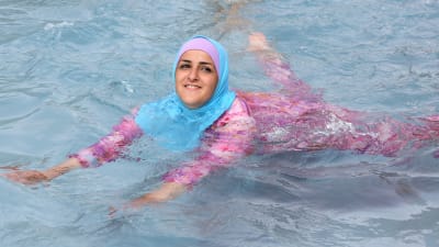 En turkisk ung kvinna simmar iklädd täckande burkini.