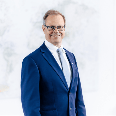 Mies sinisessä puvussa, vaaleansininen solmio. Hymyilee kameralle.