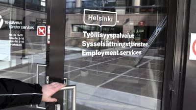 En person med handen på dörrhandtaget vid Arbets- och näringsbyrån i Helsingfors.