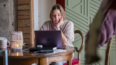 En kvinna sitter och jobbar på sin laptop i ett vardagsrum.