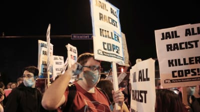 Man som bär munskydd håller upp skylt med budskapet ''fängsla alla mördarpoliser'' under demonstration i USA.