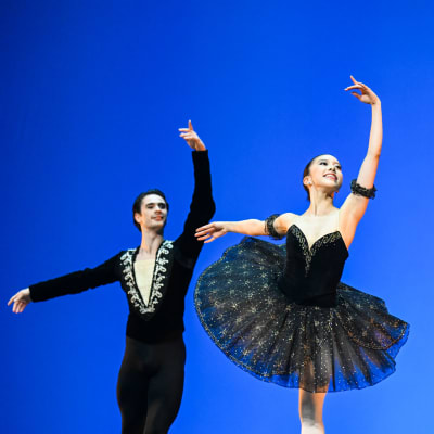 Clark Eselgroth och Yuka Masumoto i mörka kläder dansar balett mot blå bakgrund.