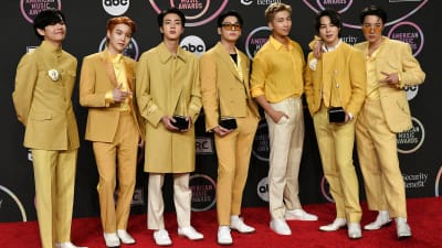 Sydkoreanska popbandet BTS sju medlemmar står på rad på röda matta, iklädda matchande gula kostymer.