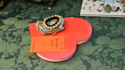 På ett bord ligger en anteckningsbok format som ett rött hjärta. Ovanpå den finns en liten portmonnä och ett armband samt en lapp där det står God jul! 10 år.